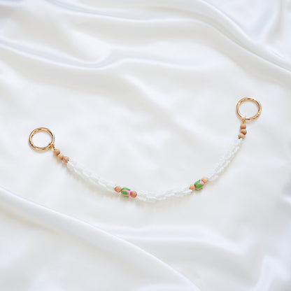 Delicate bag lei featuring white crown flower and two pink rose beads with gold rings on each end on a white fabric background