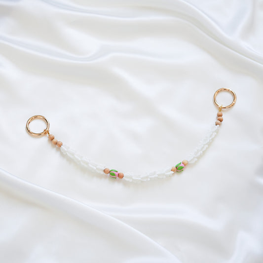 Delicate bag lei featuring white crown flower and two pink rose beads with gold rings on each end on a white fabric background