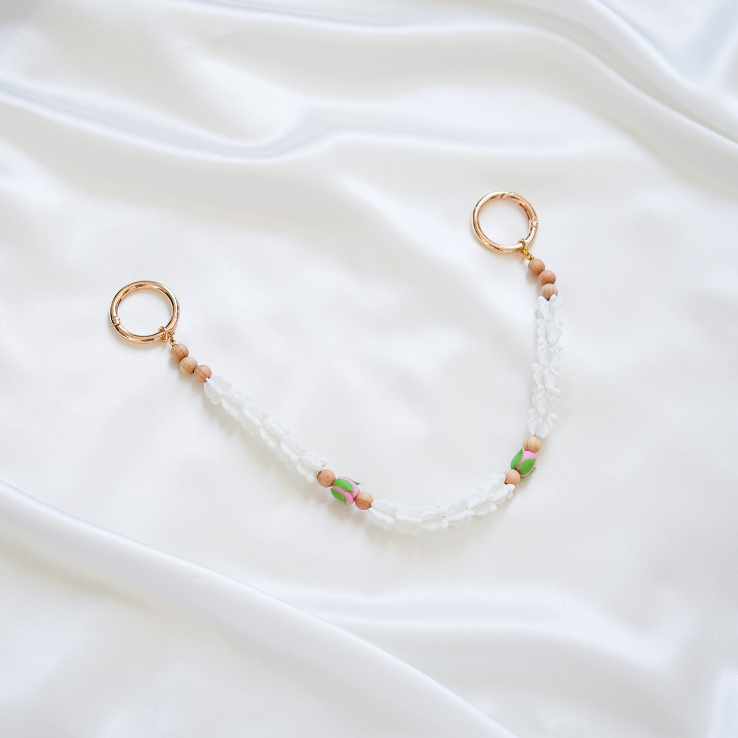 Delicate bag lei featuring white crown flower and two pink rose beads with gold rings on each end on a white fabric background