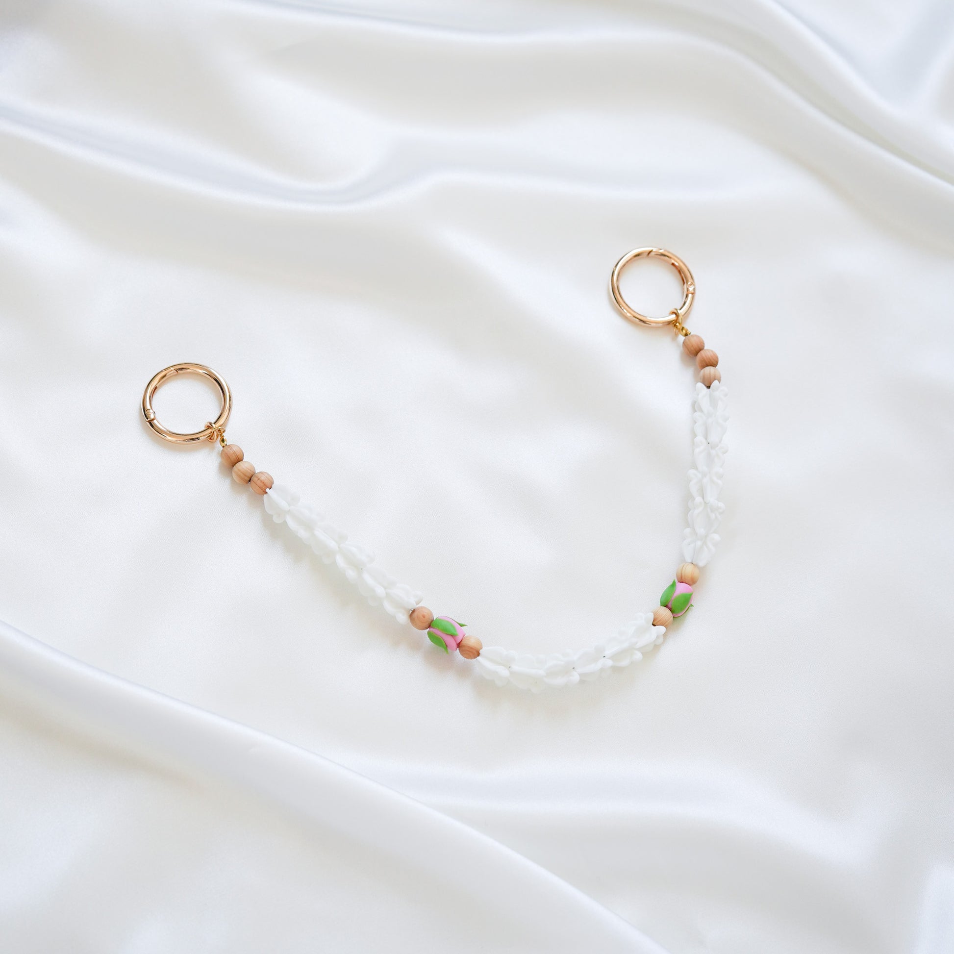 Delicate bag lei featuring white crown flower and two pink rose beads with gold rings on each end on a white fabric background