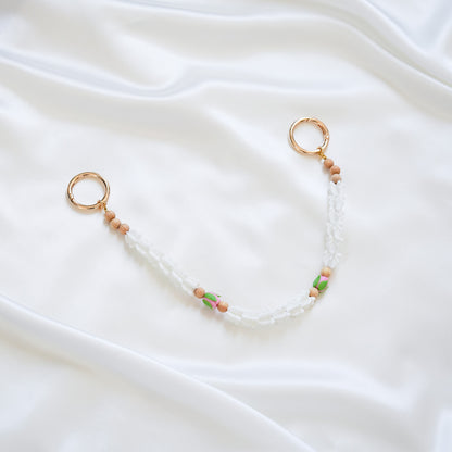 Delicate bag lei featuring white crown flower and two pink rose beads with gold rings on each end on a white fabric background