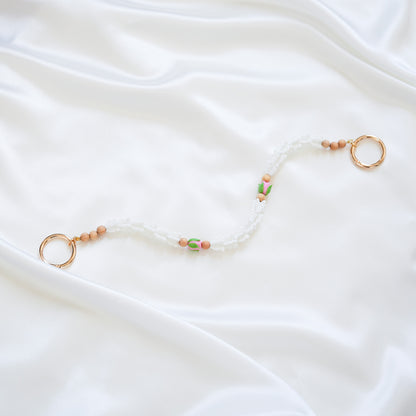 Delicate bag lei featuring white crown flower and two pink rose beads with gold rings on each end on a white fabric background