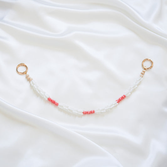 Delicate bag lei featuring white crown flower beads and small pink rose beads alternating with gold rings on each end on a white fabric background