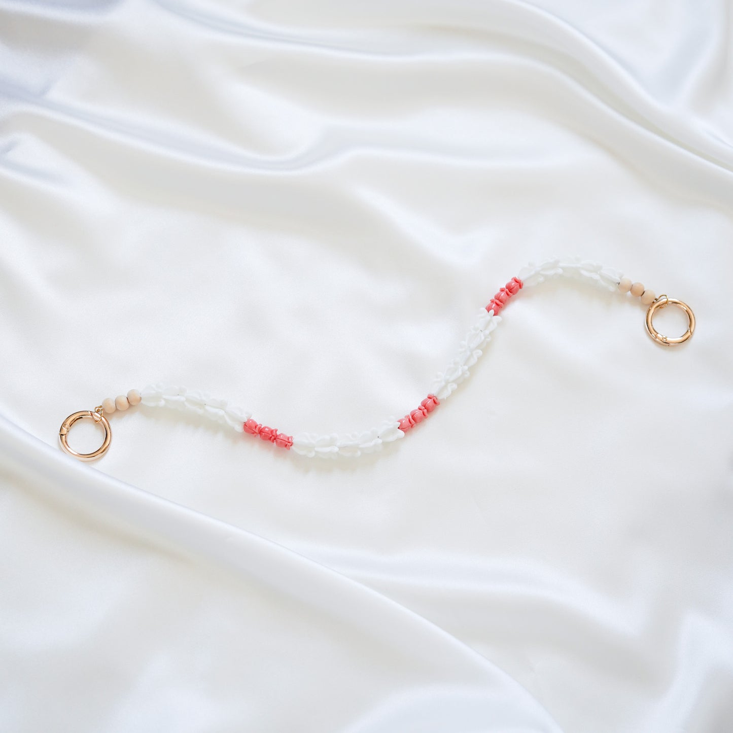 Delicate bag lei featuring white crown flower beads and small pink rose beads alternating with gold rings on each end on a white fabric background