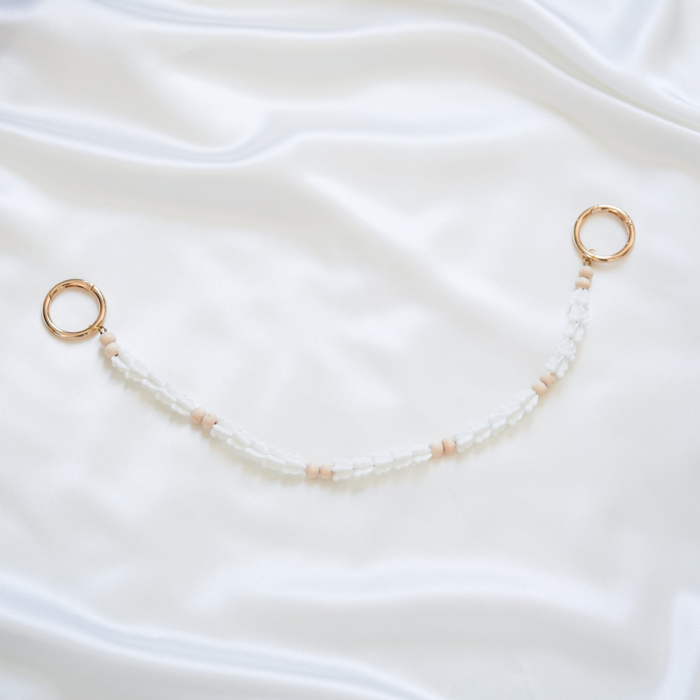 Delicate bag lei featuring white crown flower beads and light tan beads with gold rings on each end on a white fabric background