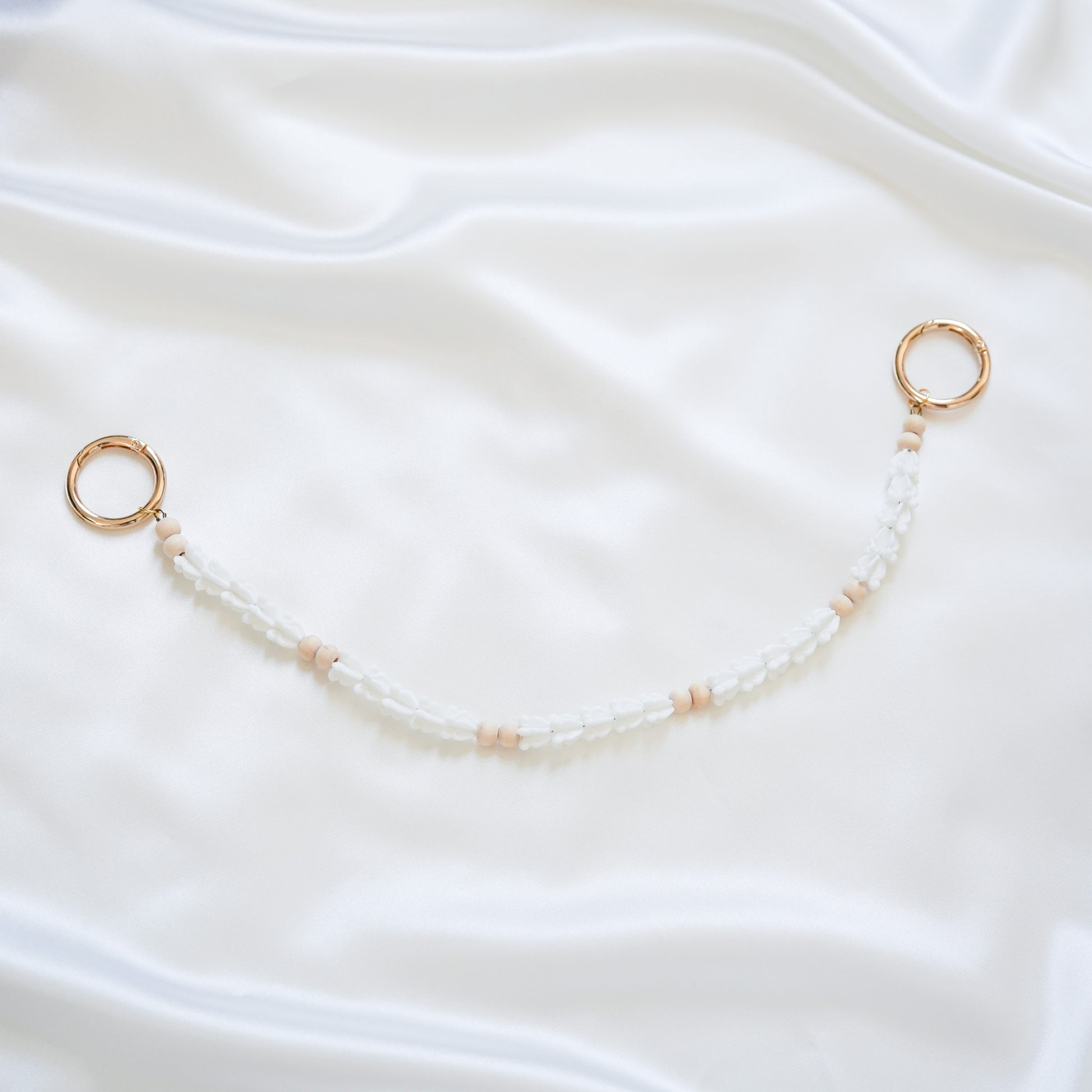 Delicate bag lei featuring white crown flower beads and light tan beads with gold rings on each end on a white fabric background