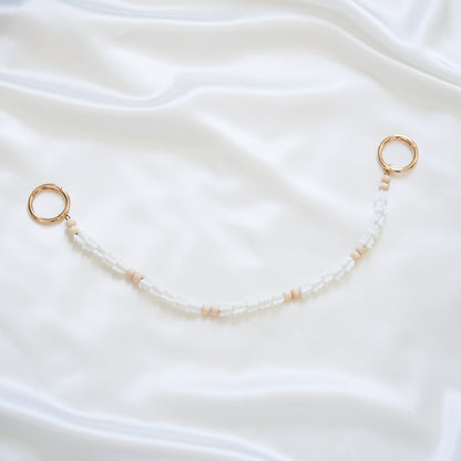 Delicate bag lei featuring white crown flower beads and light tan beads with gold rings on each end on a white fabric background