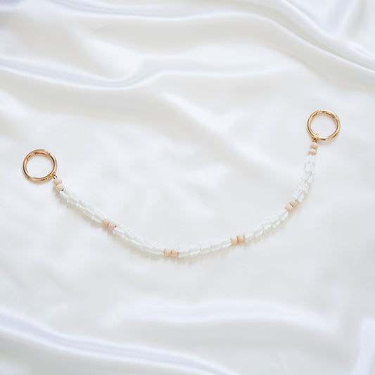 Delicate bag lei featuring white crown flower beads and light tan beads with gold rings on each end on a white fabric background