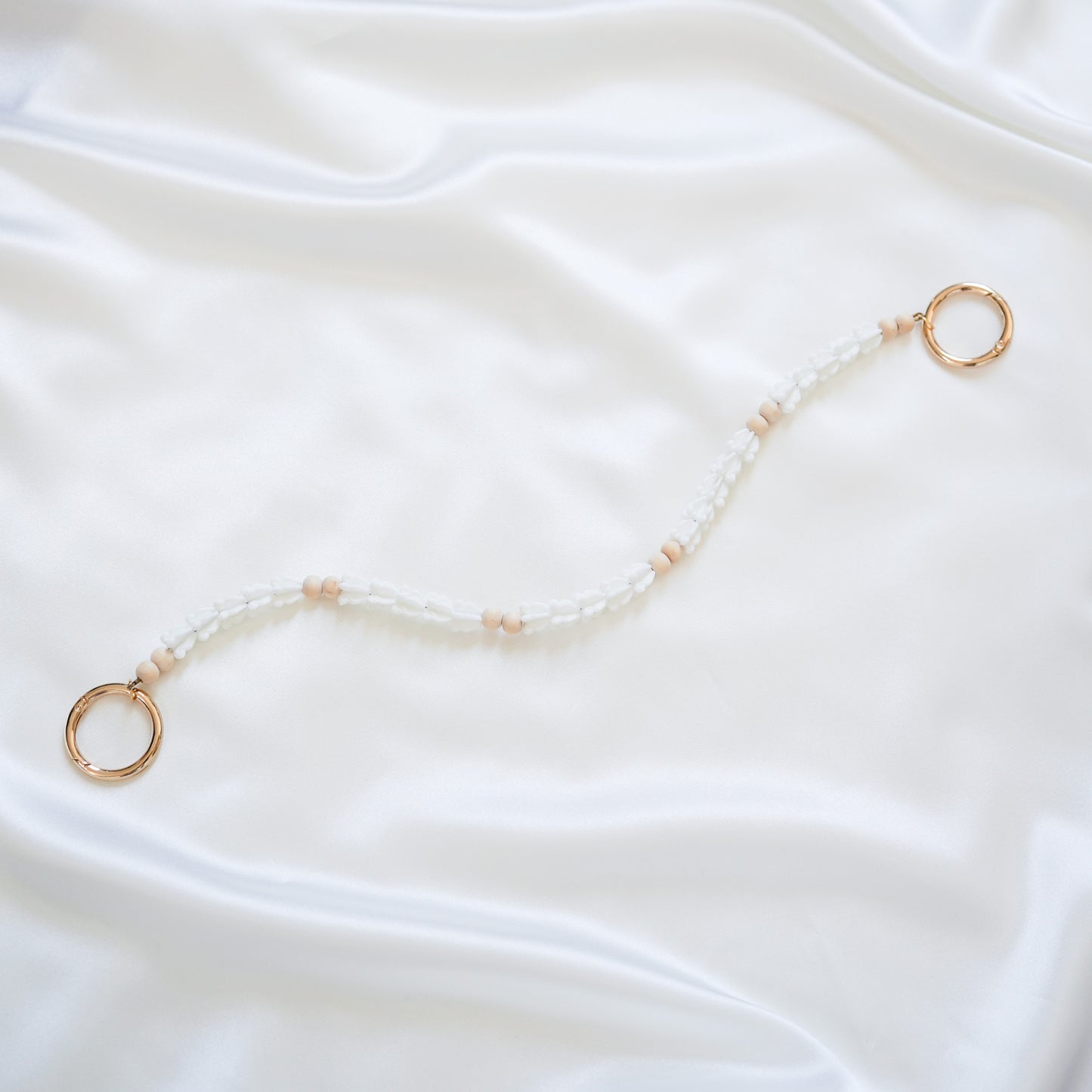 Delicate bag lei featuring white crown flower beads and light tan beads with gold rings on each end on a white fabric background