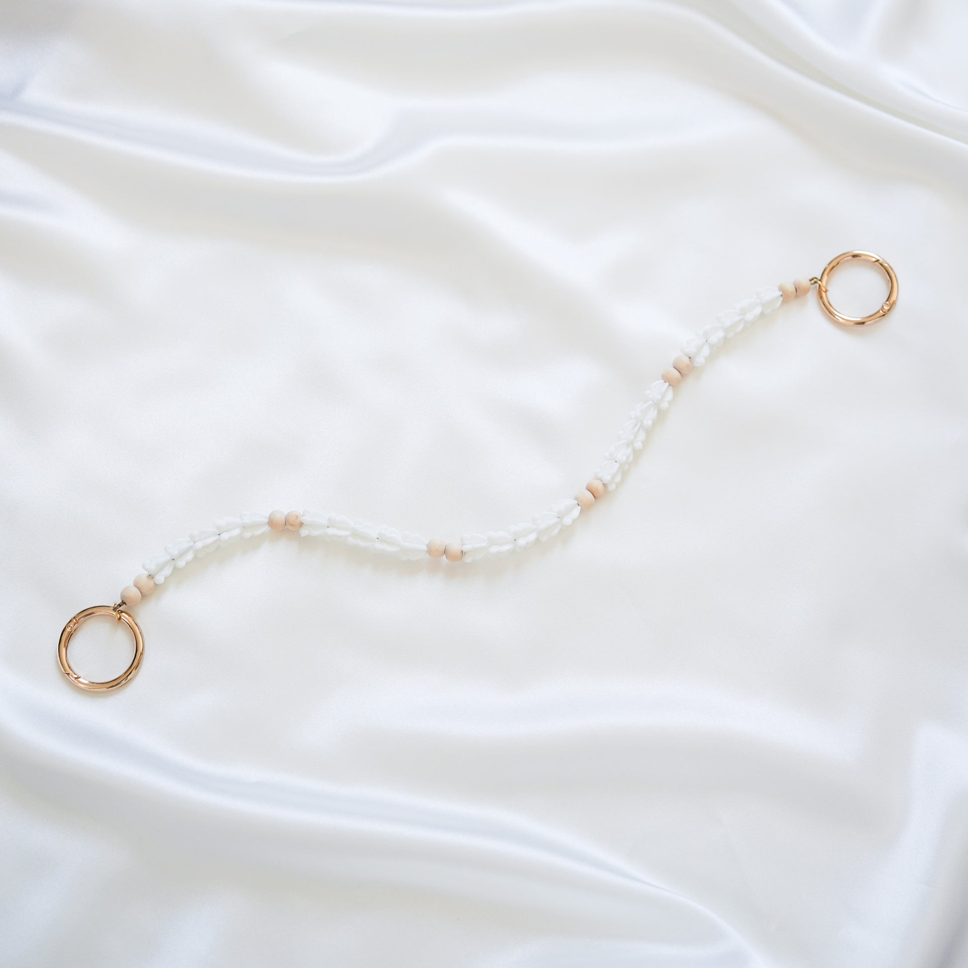 Delicate bag lei featuring white crown flower beads and light tan beads with gold rings on each end on a white fabric background