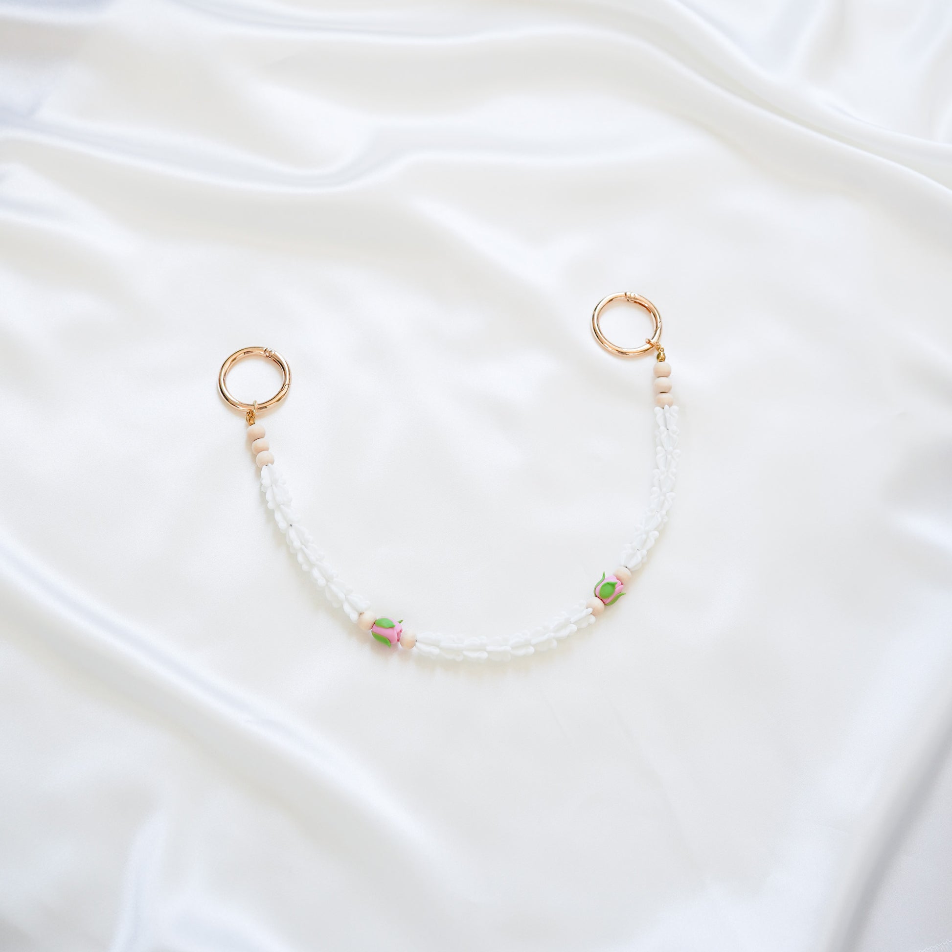 Delicate bag lei featuring white crown flower and two pink rose beads with gold rings on each end on a white fabric background