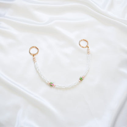 Delicate bag lei featuring white crown flower and two pink rose beads with gold rings on each end on a white fabric background