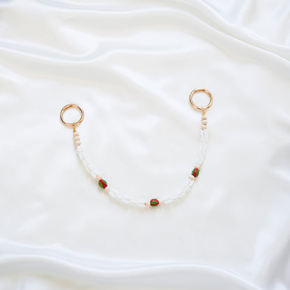 Delicate bag lei featuring white crown flower and three red rose beads with gold rings on each end on a white fabric background