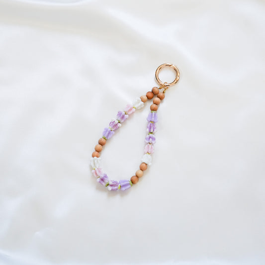 Beaded keychain with tan beads and purple, pink and white crown flower beads on a white background