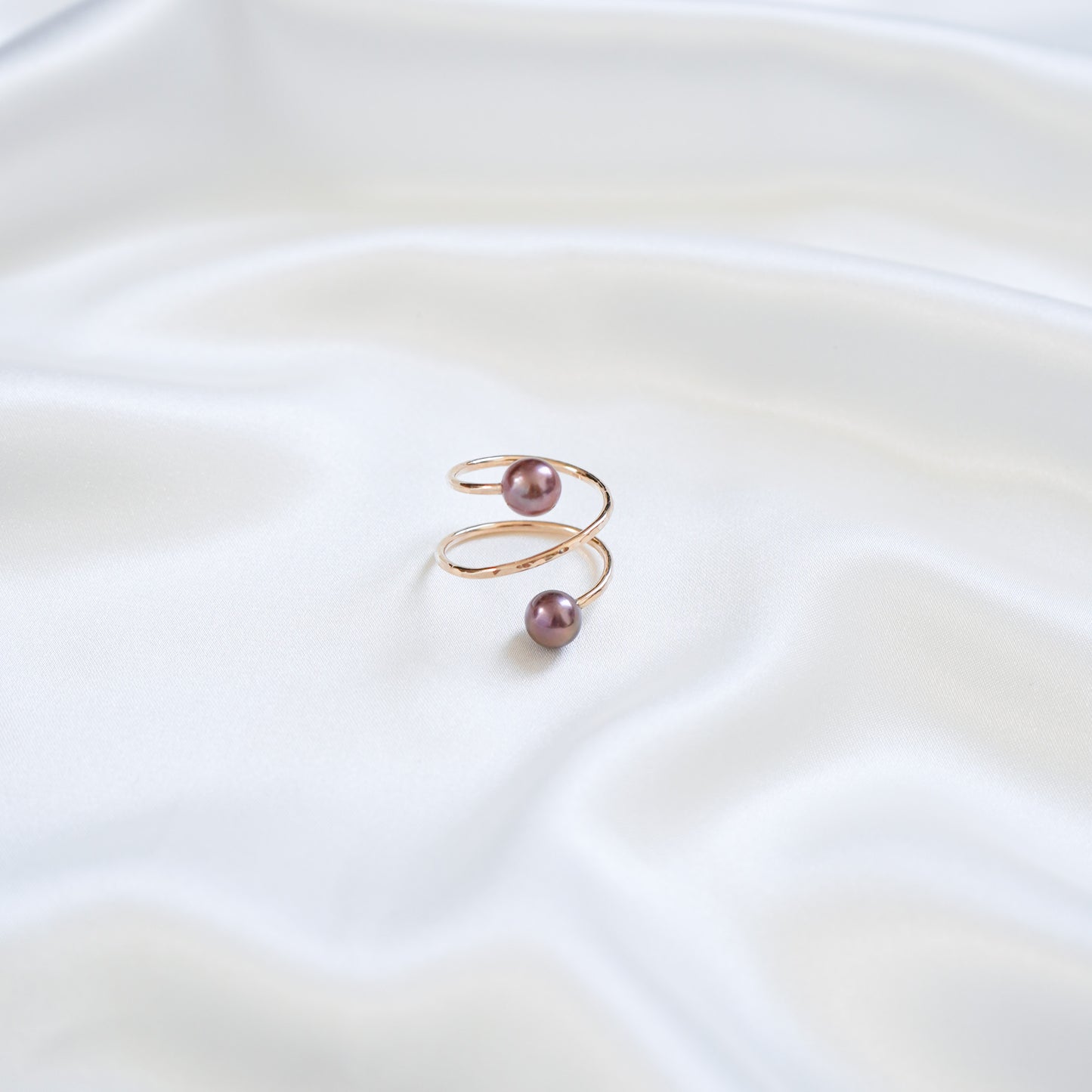Gold ring with dark pink pearls on a white fabric background