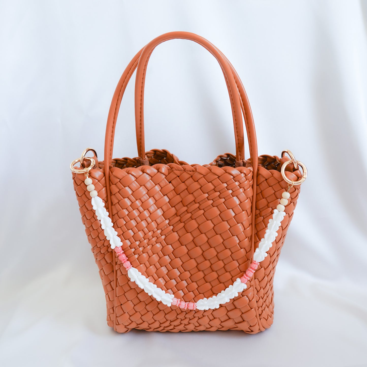 Brown woven handbag with a decorative bag lei strap on a white background