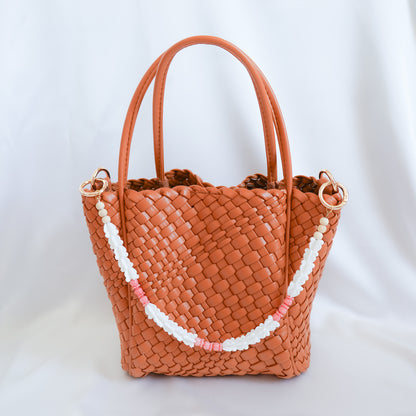 Brown woven handbag with a decorative bag lei strap on a white background