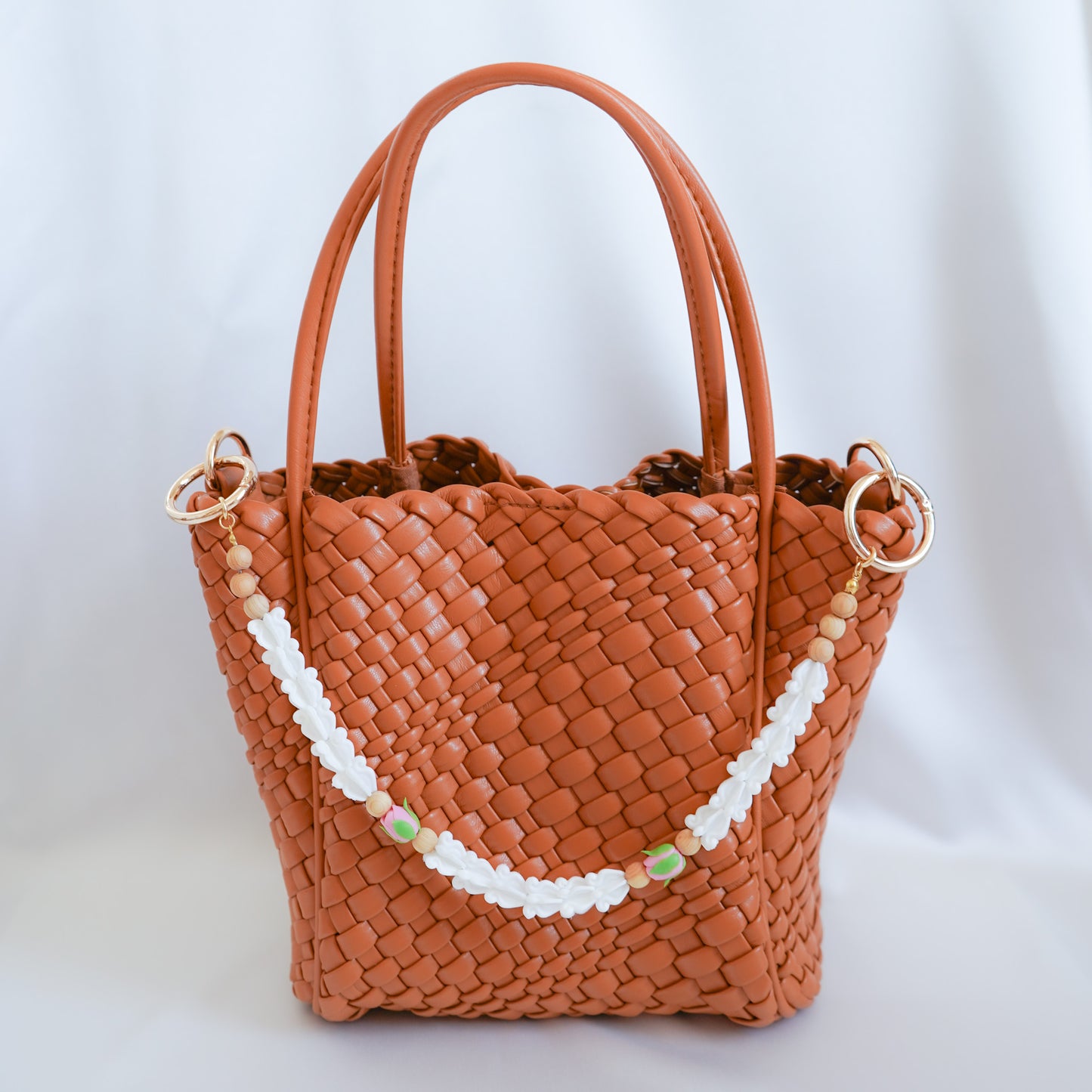 Brown woven handbag with a decorative flower bag lei strap on a white background