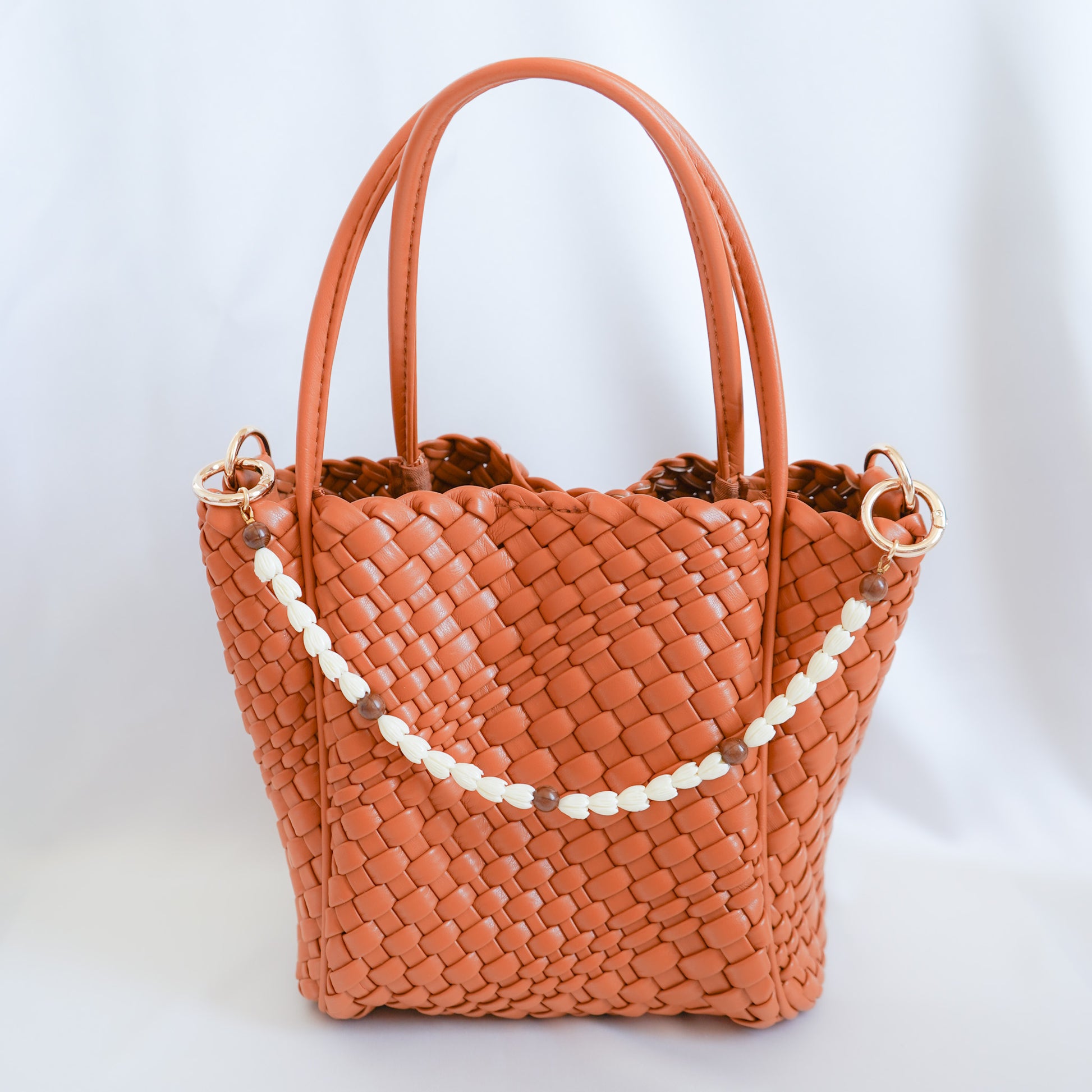 Brown woven handbag with white beaded bag lei on a white background