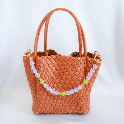 Woven handbag with decorative floral beaded lei bag strap on a white background