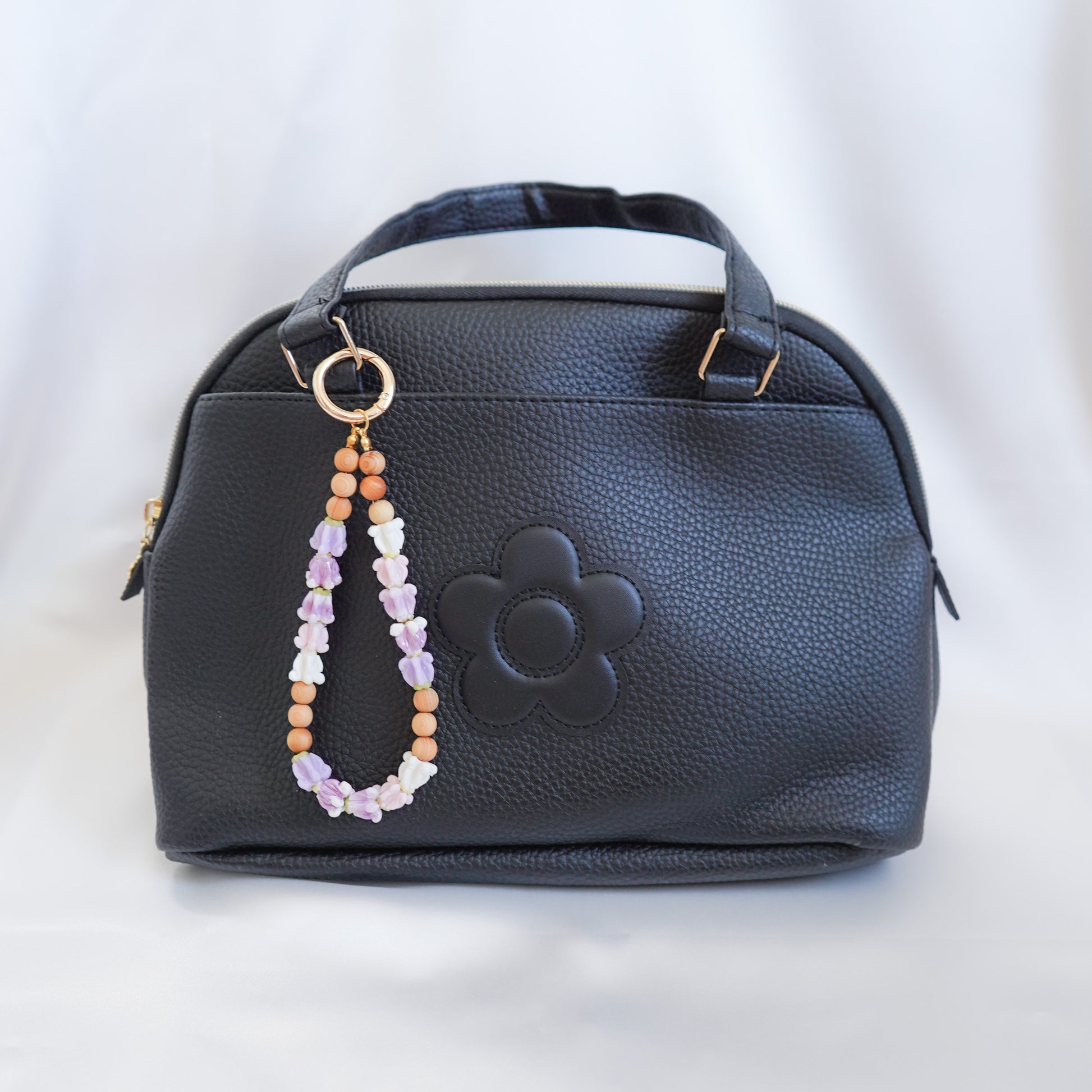 Black handbag with a beaded flower keychain on a white background