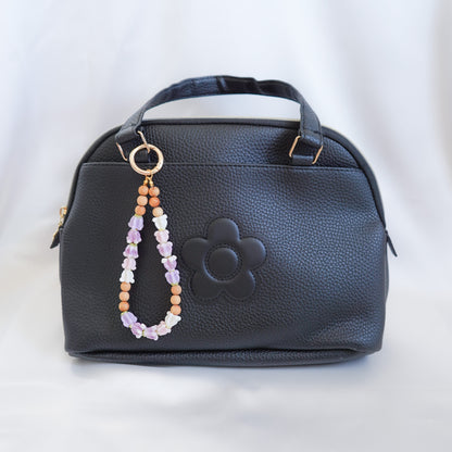 Black handbag with a beaded flower keychain on a white background