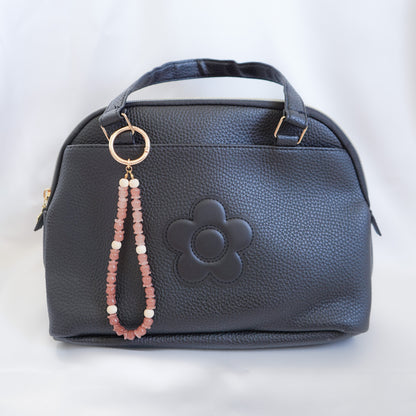 Black handbag with a floral design and a beaded strap on a white background