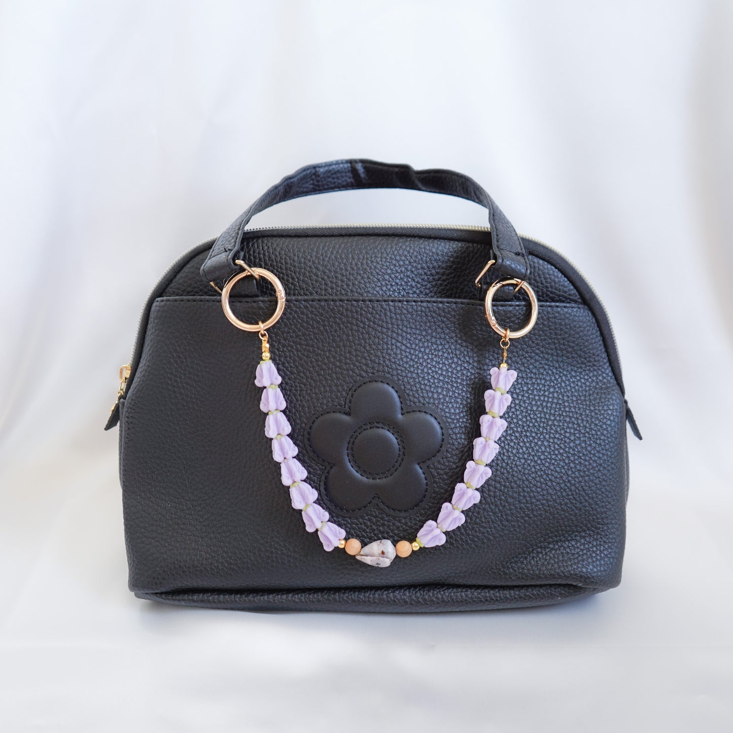 Black handbag with floral design and beaded  bag lei on the handle on a white background