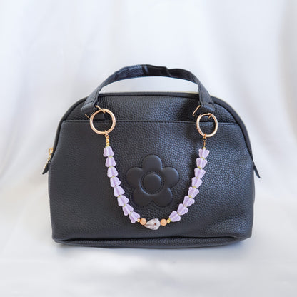 Black handbag with floral design and beaded  bag lei on the handle on a white background