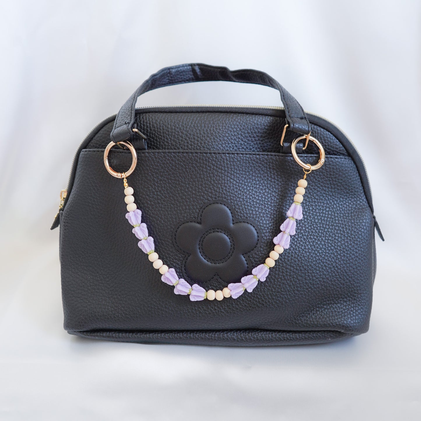 Black handbag with a decorative beaded bag lei chain on a white background