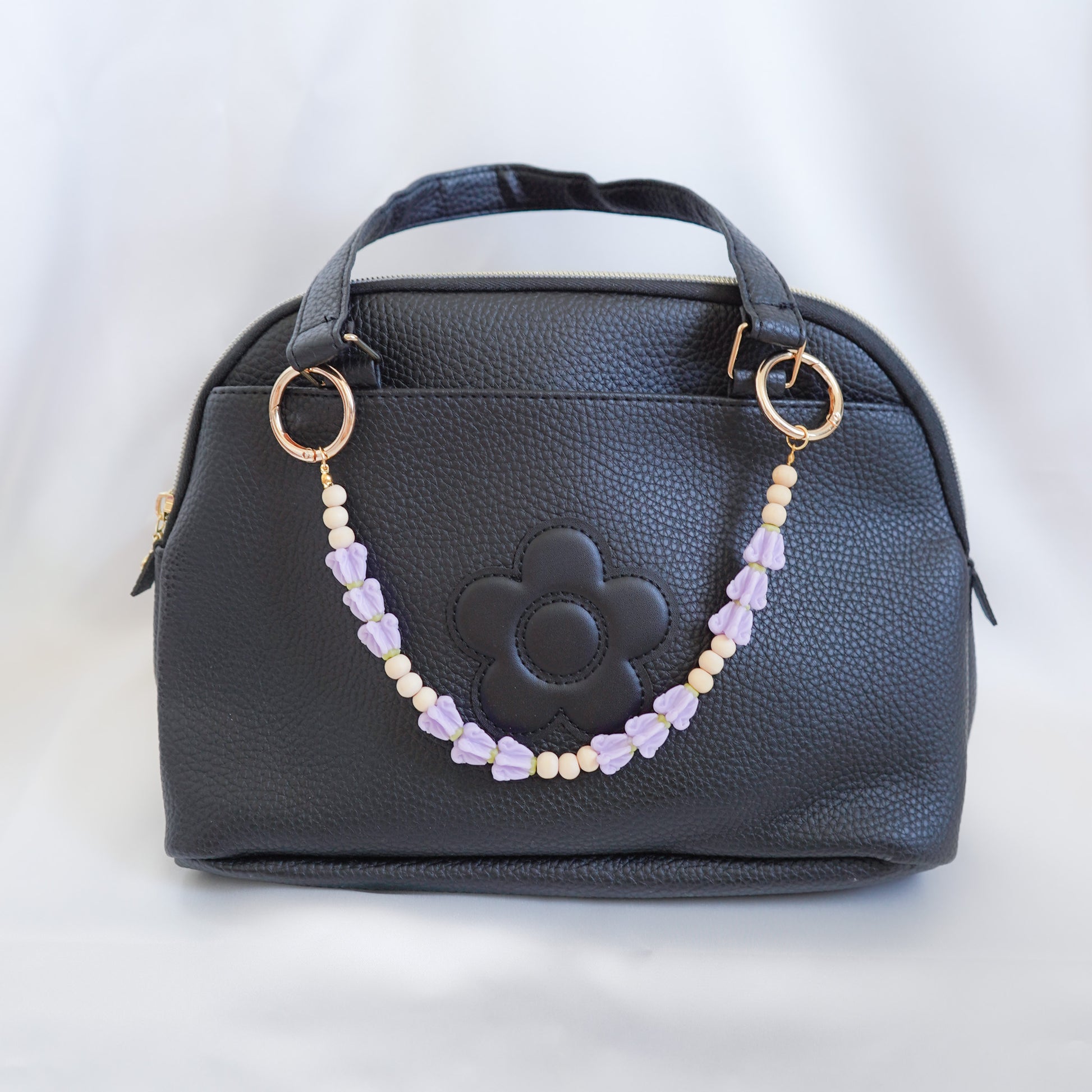 Black handbag with a decorative beaded bag lei chain on a white background