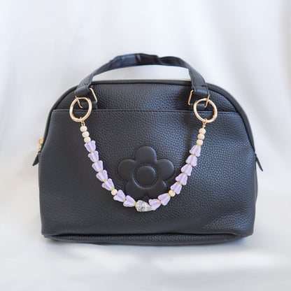 Black handbag with a decorative purple beaded bag lei strap on a white background
