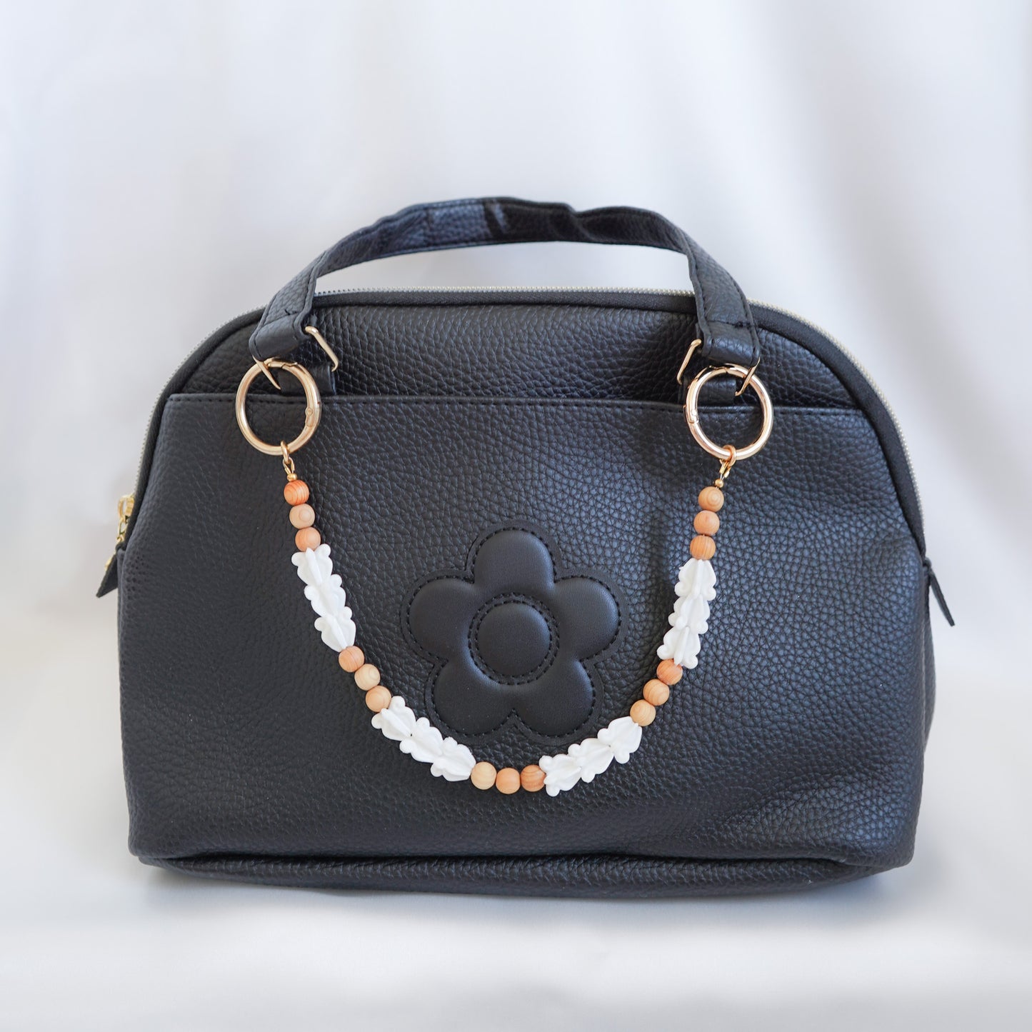 Black handbag with a decorative beaded bag lei strap on a white background