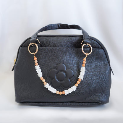Black handbag with a decorative beaded bag lei strap on a white background
