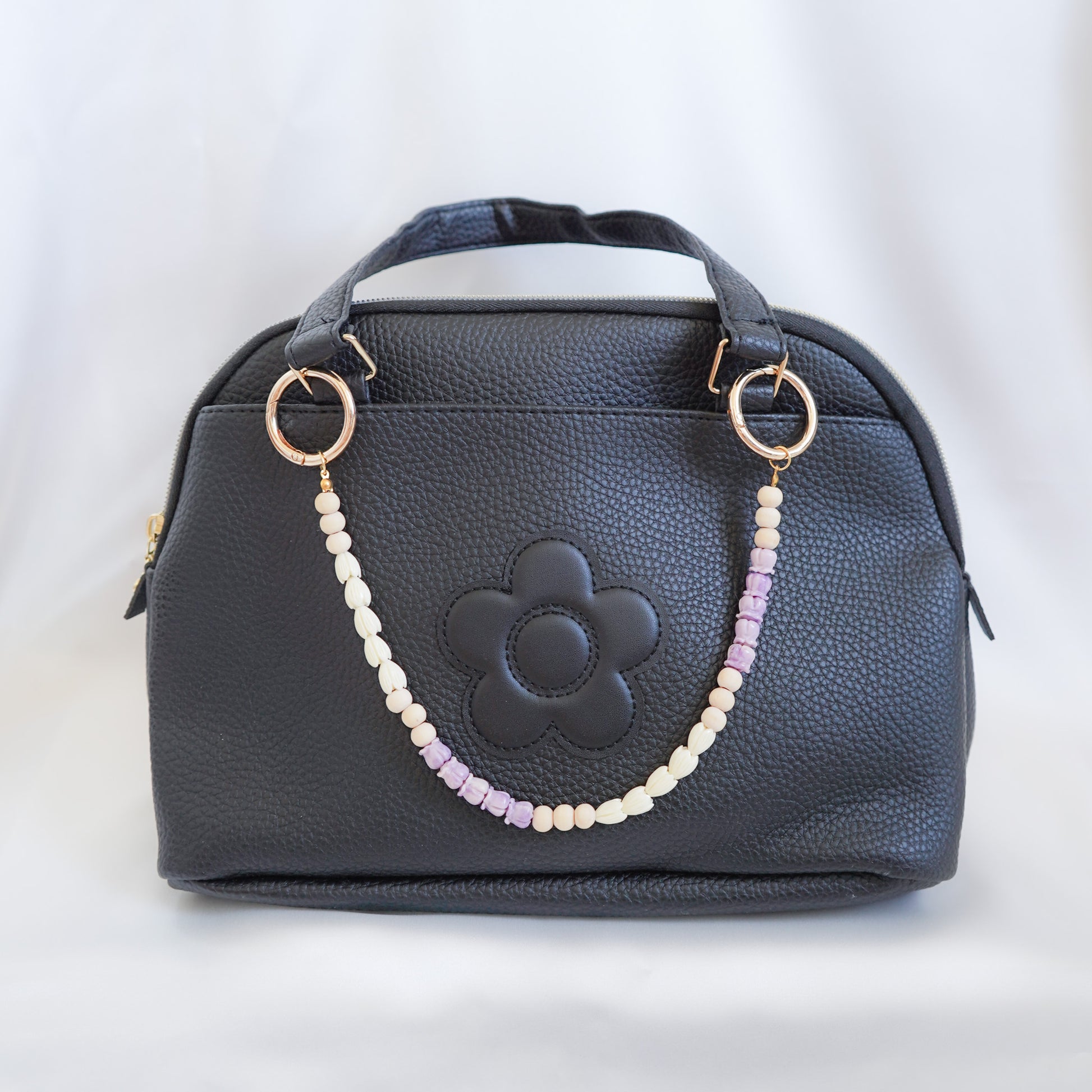Black handbag with a floral design and beaded bag lei on the handle on a white background