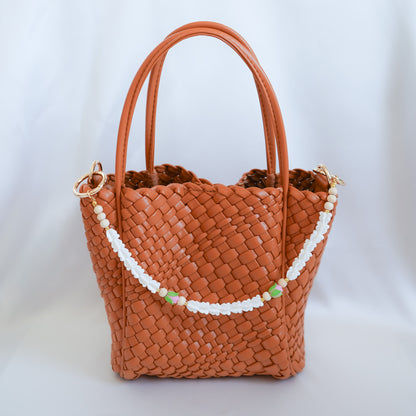 Brown woven handbag with floral beaded bag lei strap on a white background