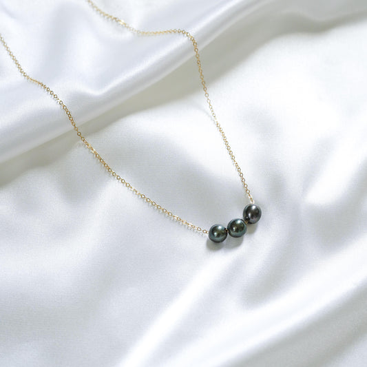 Necklace with three tahitian pearls on a gold chain against a white fabric background