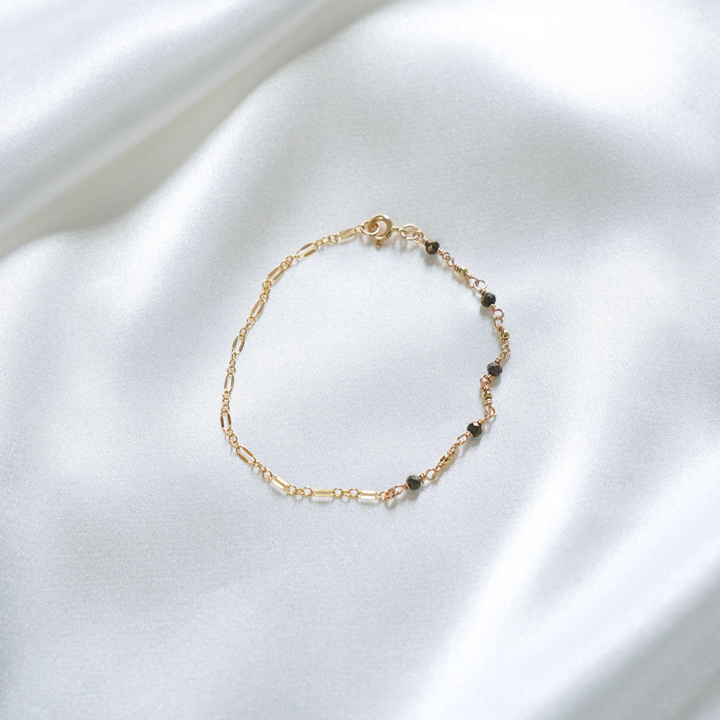 Gold bracelet with small black beads on a white fabric background