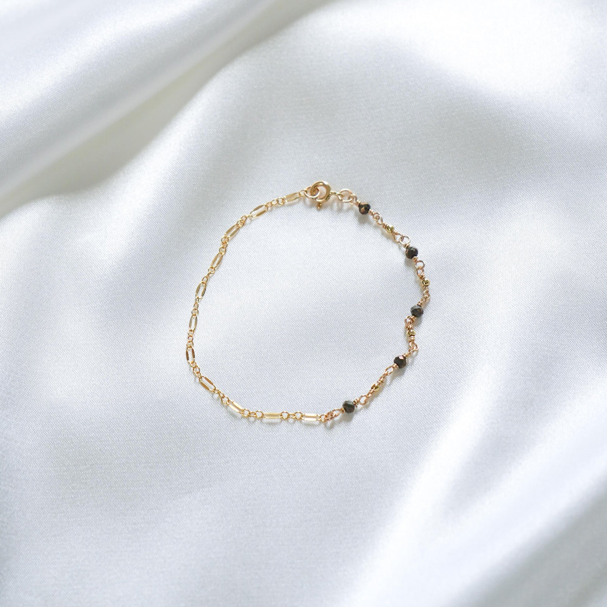 Gold bracelet with small black beads on a white fabric background