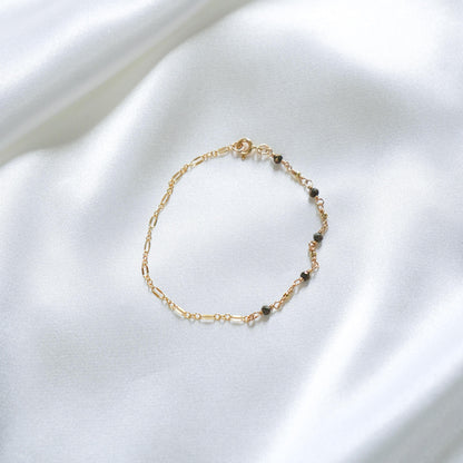 Gold bracelet with small black beads on a white fabric background