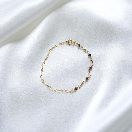 Gold bracelet with small black beads on a white fabric background