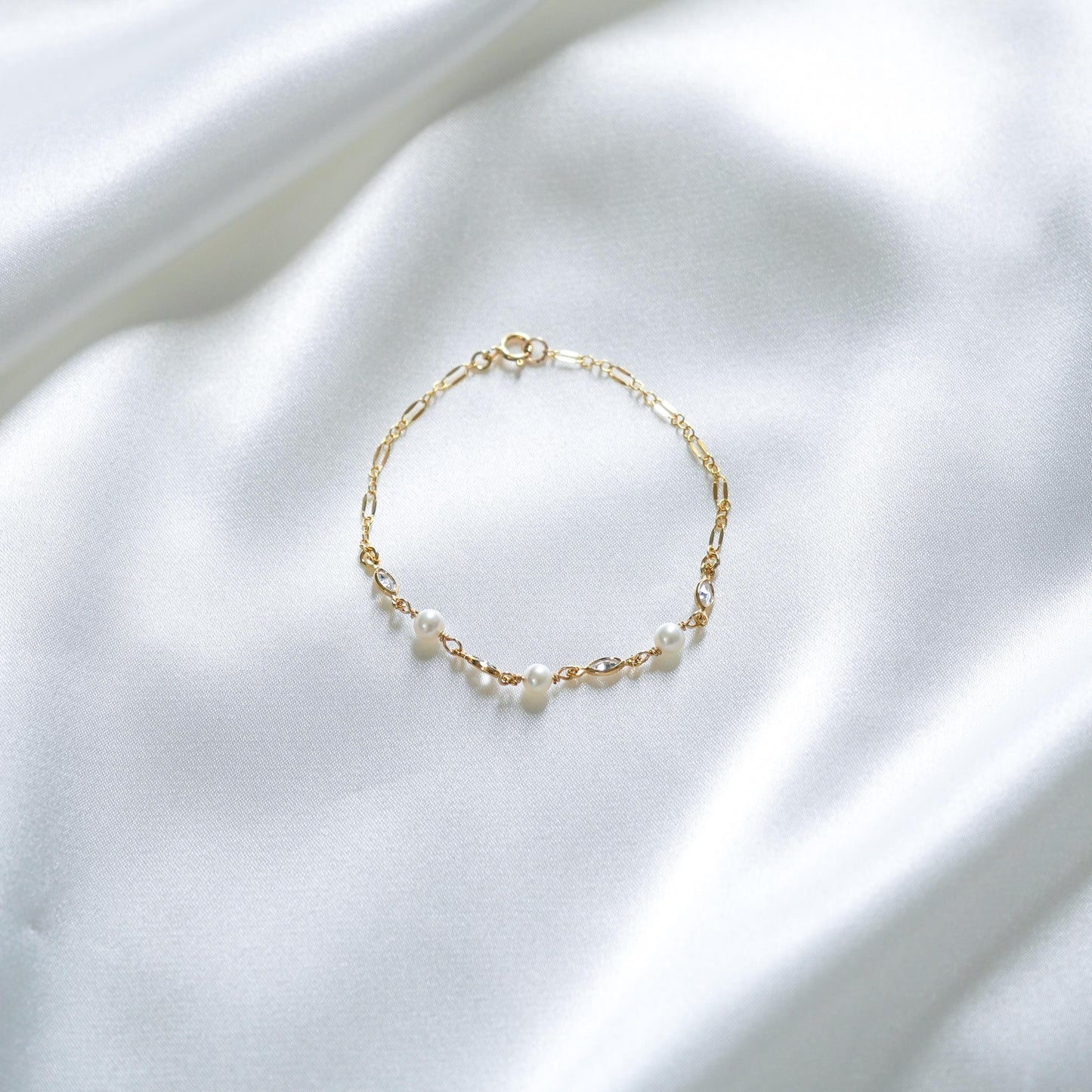 Gold bracelet with white pearls and cz stones on a white fabric background