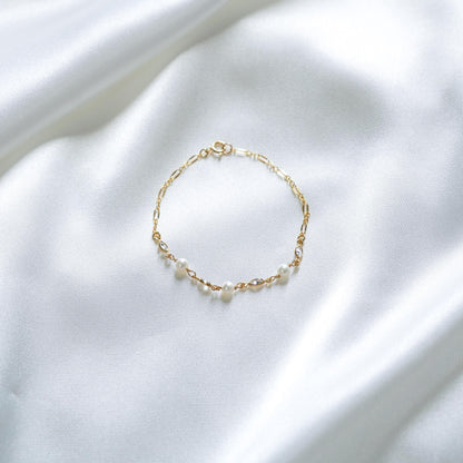 Gold bracelet with white pearls and cz stones on a white fabric background