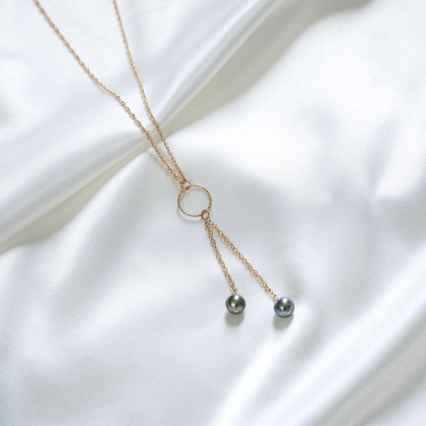 Delicate necklace with gold circle charm and two hanging pearls on a white fabric background