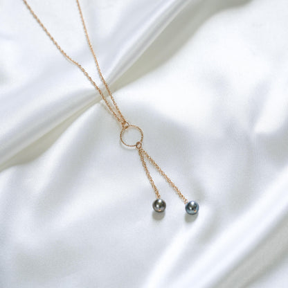 Delicate necklace with gold circle charm and two hanging pearls on a white fabric background