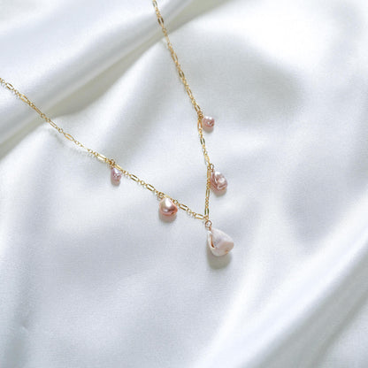 Delicate gold necklace with pink keshi pearls and a white shell on a white fabric background