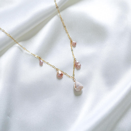 Delicate gold necklace with pink keshi pearls and a white shell on a white fabric background