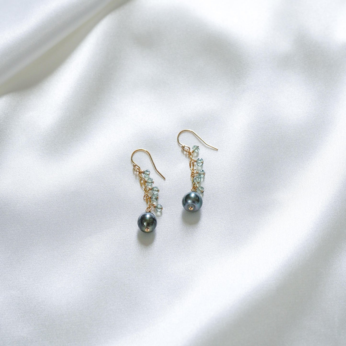 Pair of earrings with pearls and blue gemstones on a white fabric background