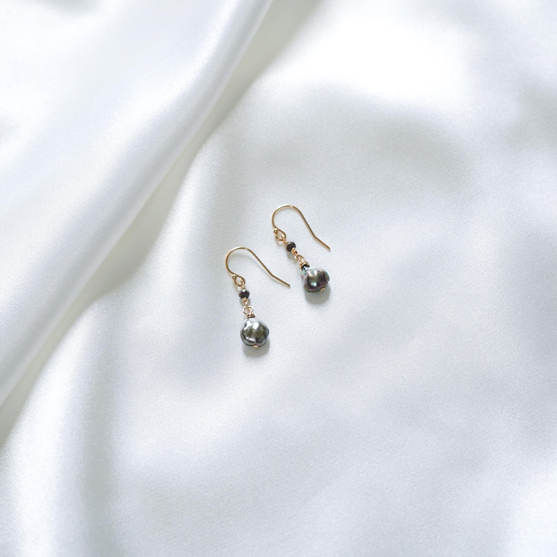 Pair of pearl earrings with black spinel bead on a white fabric background