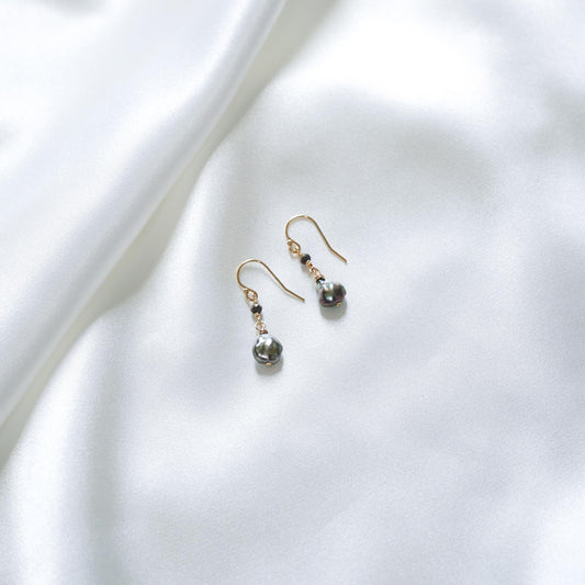 Pair of pearl earrings with black spinel bead on a white fabric background